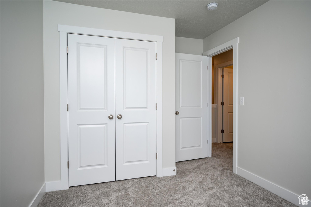 Unfurnished bedroom with a closet, light carpet, and a textured ceiling