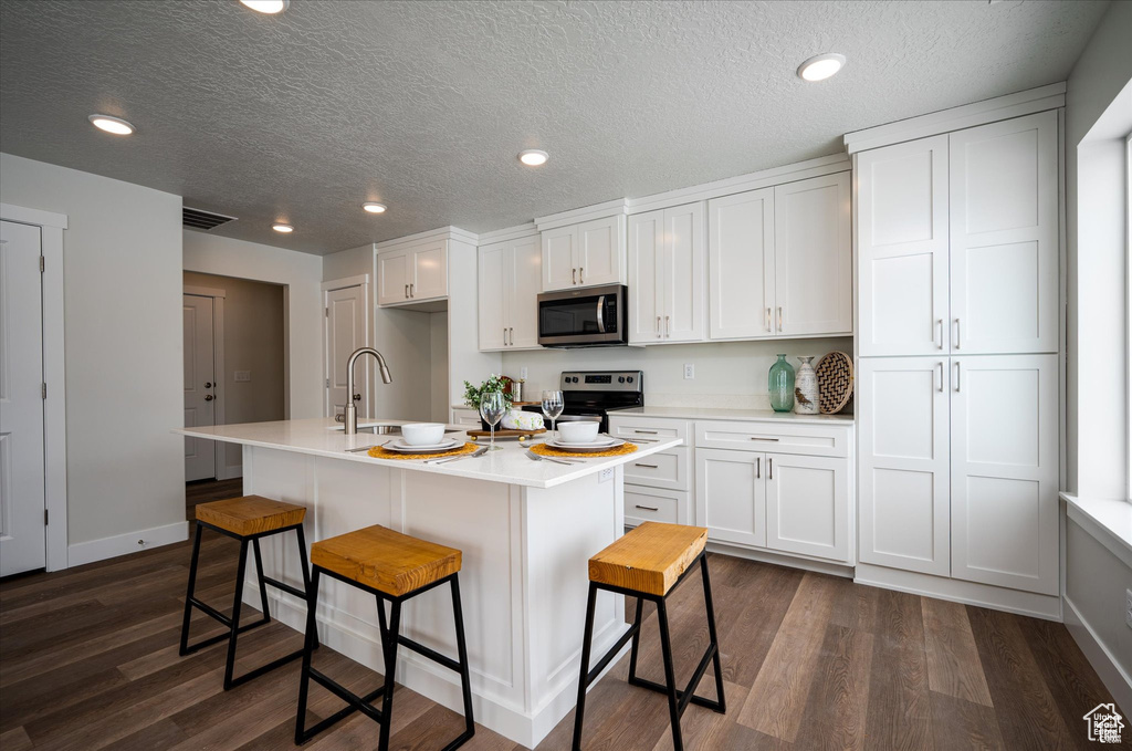 Kitchen with a breakfast bar, appliances with stainless steel finishes, white cabinetry, and an island with sink