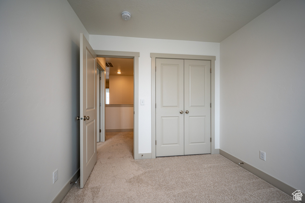 Unfurnished bedroom featuring light carpet and a closet