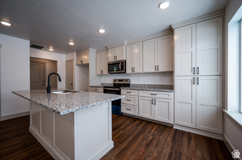 Kitchen featuring dark wood-type flooring, sink, white cabinets, appliances with stainless steel finishes, and light stone counters