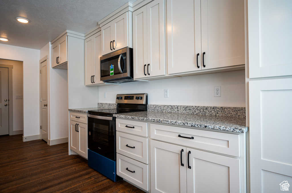 Kitchen featuring dark hardwood / wood-style floors, stainless steel appliances, light stone countertops, white cabinetry, and a textured ceiling