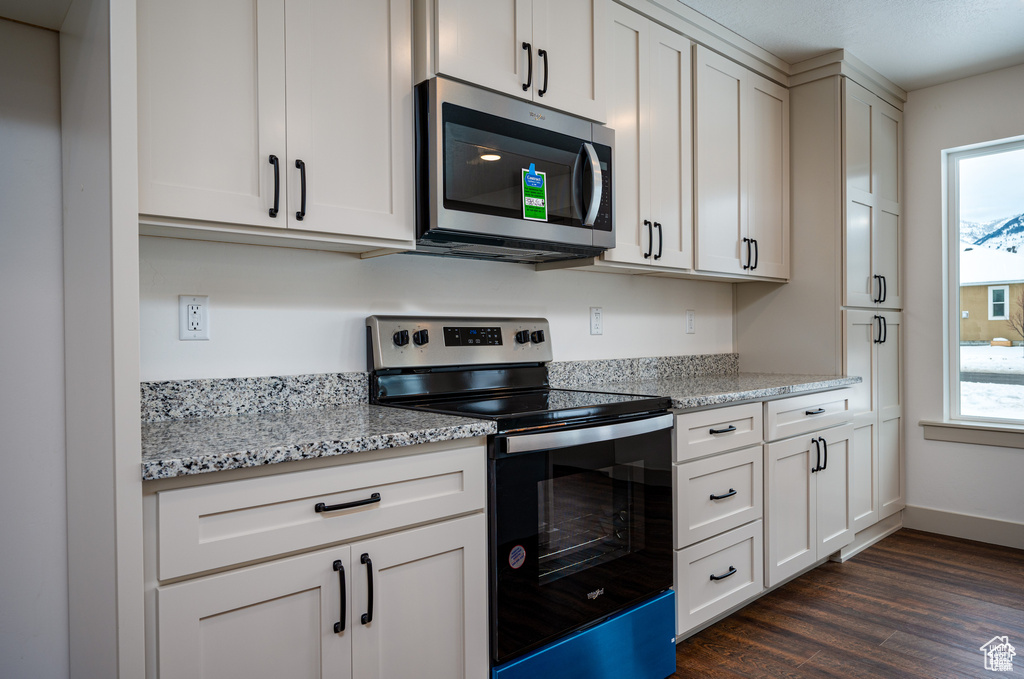 Kitchen featuring dark wood-type flooring, light stone countertops, appliances with stainless steel finishes, and white cabinetry