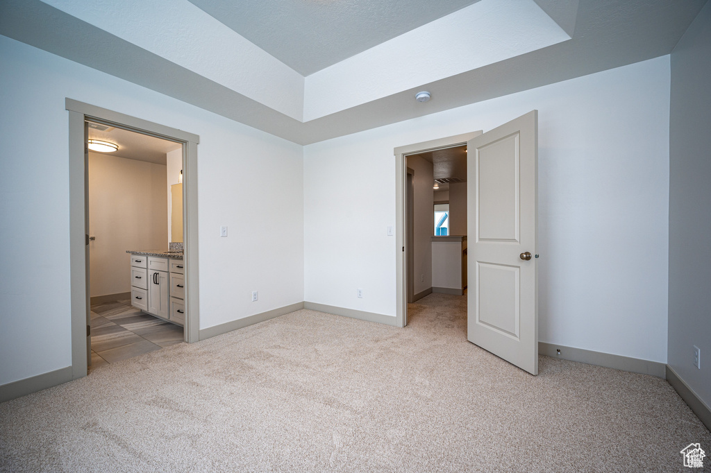 Unfurnished bedroom with ensuite bathroom and light colored carpet