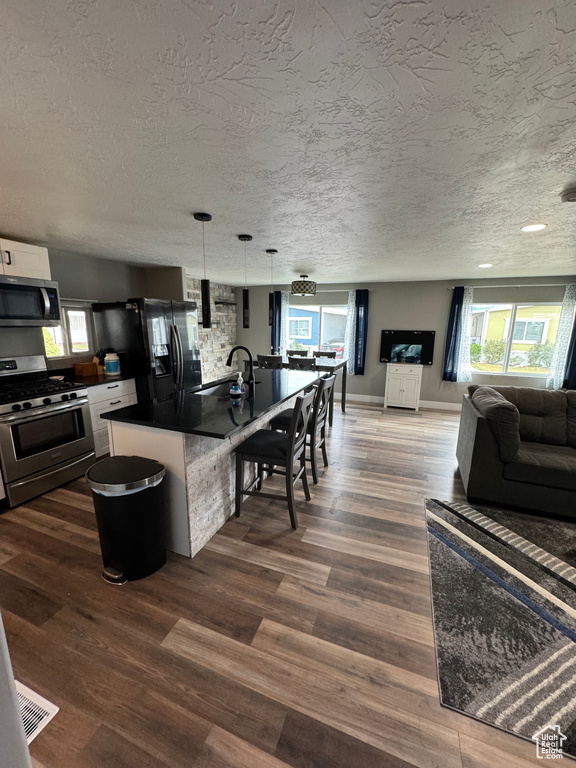 Kitchen with a textured ceiling, stainless steel appliances, pendant lighting, white cabinets, and a breakfast bar