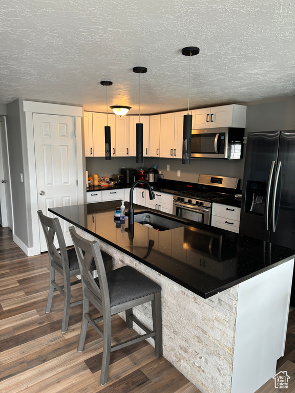 Kitchen with appliances with stainless steel finishes, hanging light fixtures, dark hardwood / wood-style floors, a breakfast bar area, and a center island with sink