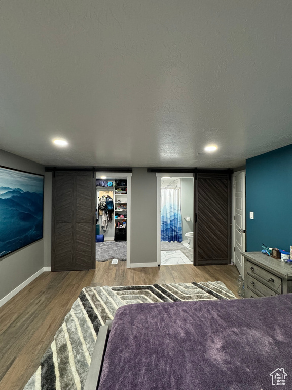 Unfurnished bedroom featuring connected bathroom, a textured ceiling, a barn door, and wood-type flooring