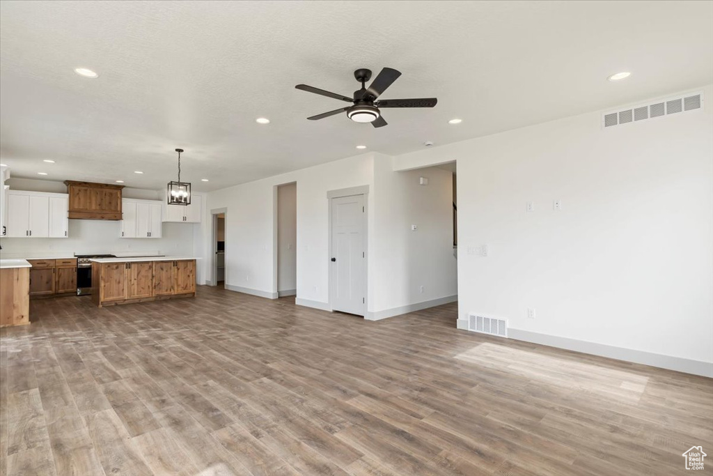 Unfurnished living room featuring a textured ceiling, ceiling fan with notable chandelier, and light wood-type flooring