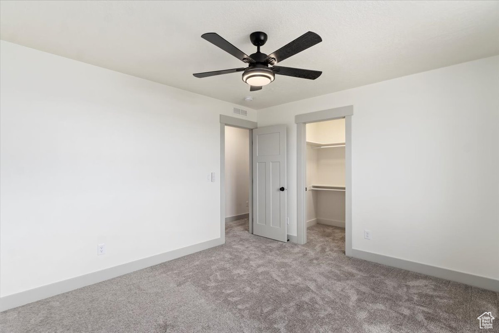 Unfurnished bedroom featuring light carpet, a walk in closet, a closet, and ceiling fan