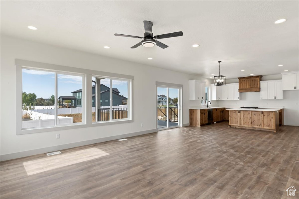 Unfurnished living room featuring sink, light hardwood / wood-style flooring, and ceiling fan with notable chandelier