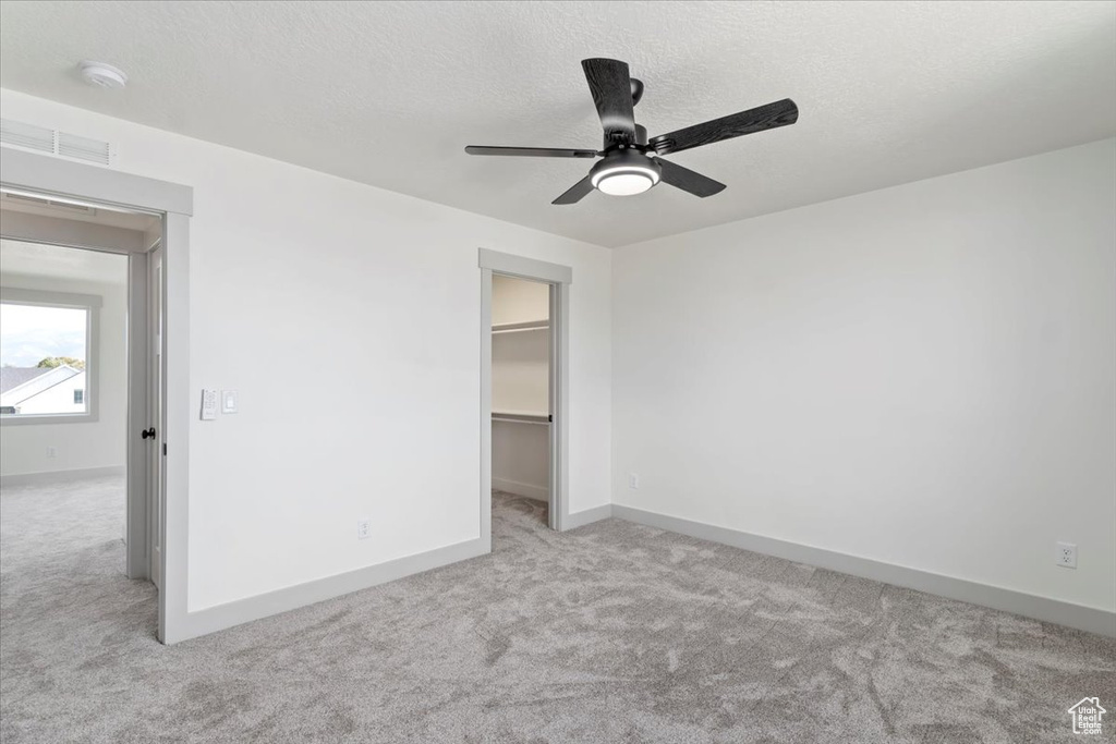 Unfurnished bedroom with a spacious closet, light carpet, a closet, and ceiling fan