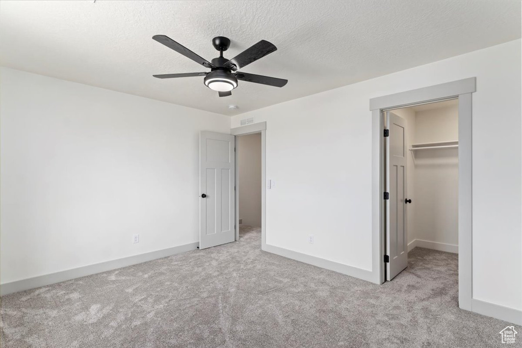 Unfurnished bedroom featuring light carpet, ceiling fan, a textured ceiling, a closet, and a walk in closet