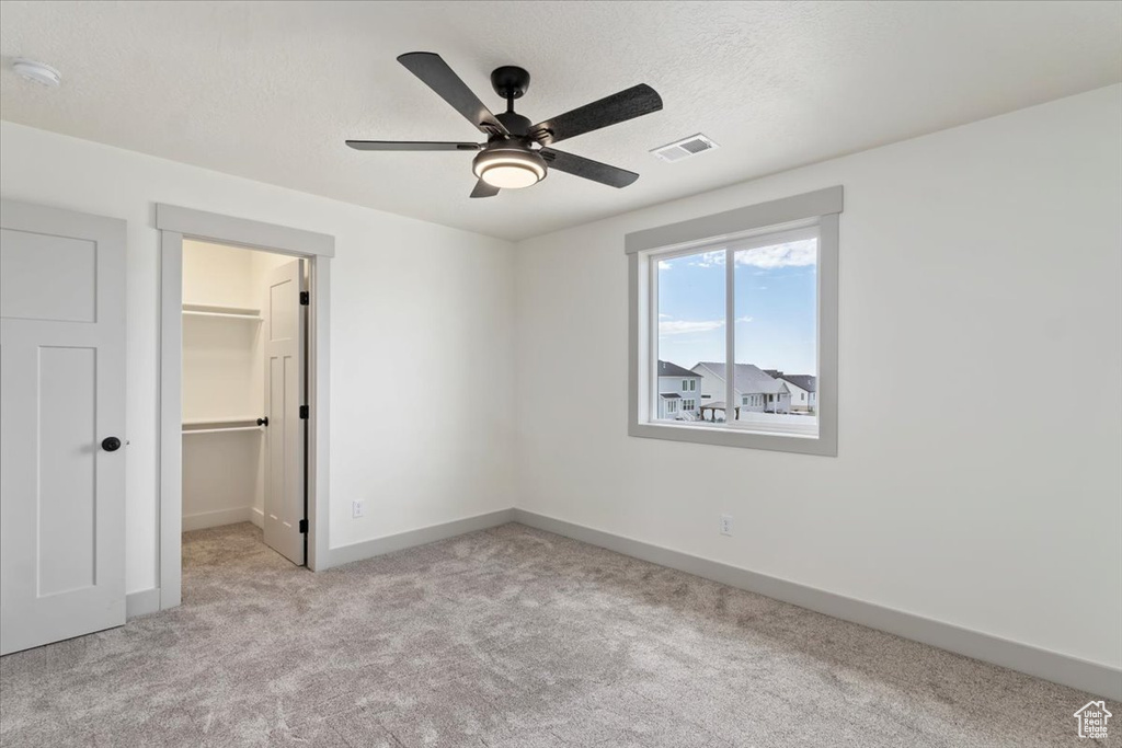 Unfurnished bedroom with ceiling fan, a textured ceiling, a spacious closet, a closet, and light colored carpet