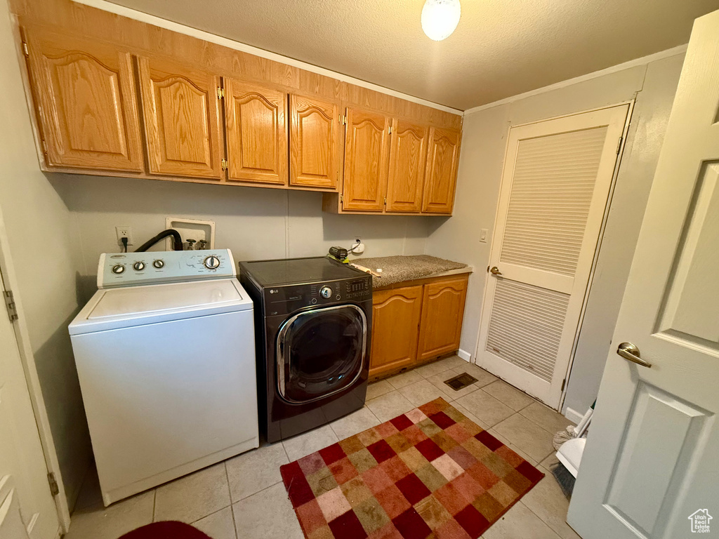 Clothes washing area featuring cabinets, a textured ceiling, washing machine and dryer, and light tile patterned floors