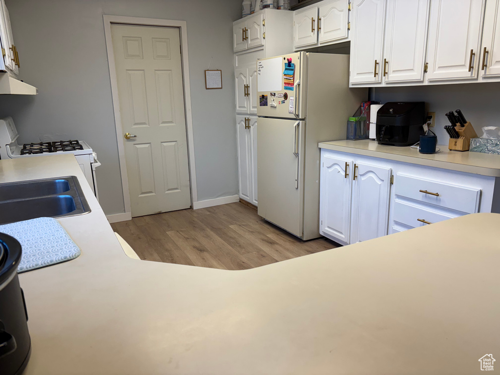 Kitchen featuring white cabinets, exhaust hood, light hardwood / wood-style flooring, sink, and white appliances