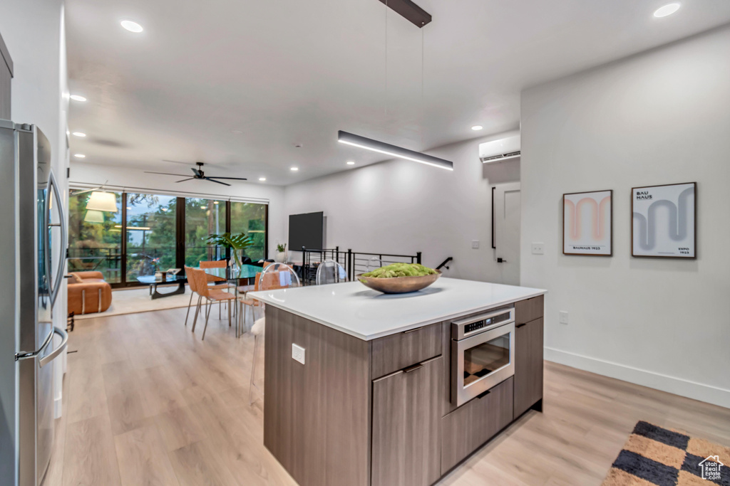 Kitchen with a kitchen island, hanging light fixtures, light wood-type flooring, appliances with stainless steel finishes, and ceiling fan