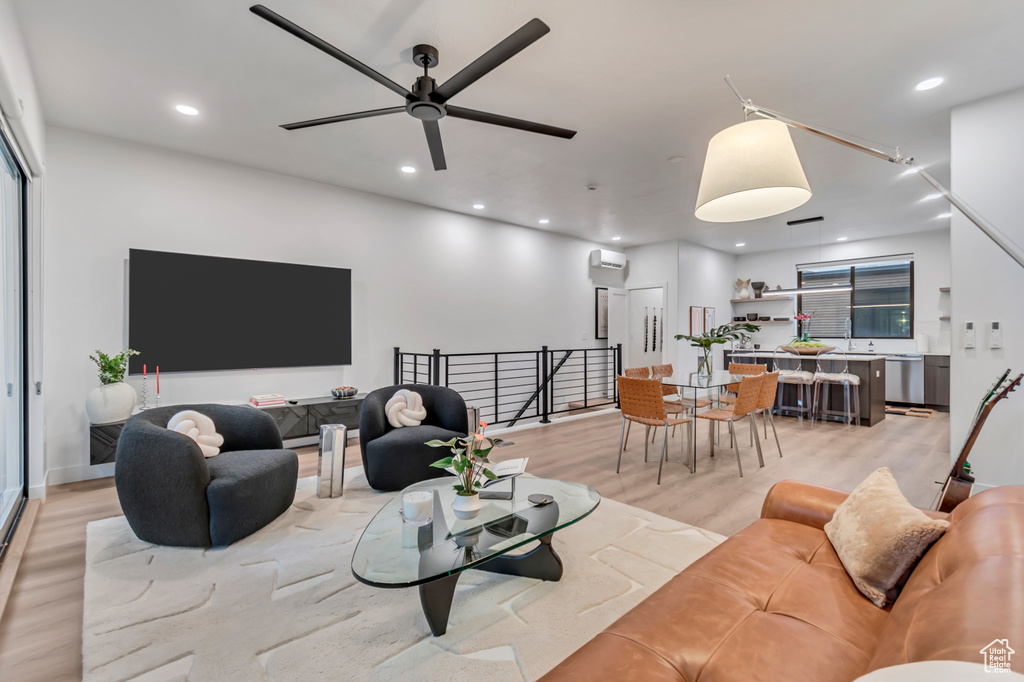 Living room with ceiling fan, a wall mounted AC, and light hardwood / wood-style flooring