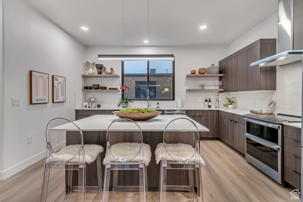 Kitchen featuring a kitchen breakfast bar, wall chimney range hood, light hardwood / wood-style floors, and double oven range