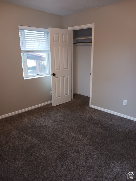 Unfurnished bedroom featuring a closet and dark carpet