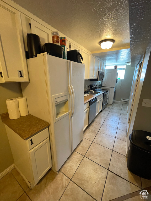 Kitchen featuring a textured ceiling, white cabinetry, stainless steel appliances, and light tile patterned flooring