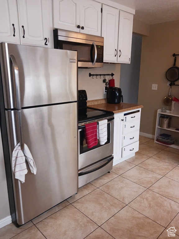 Kitchen featuring appliances with stainless steel finishes, light tile patterned flooring, and white cabinets