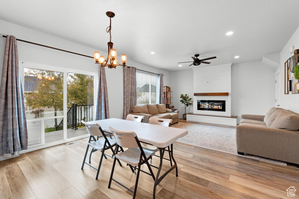 Dining space with a fireplace, ceiling fan with notable chandelier, and light wood-type flooring