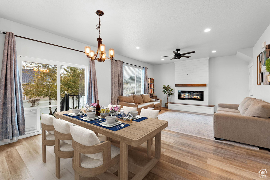 Dining space featuring light wood-type flooring, ceiling fan with notable chandelier, and a fireplace