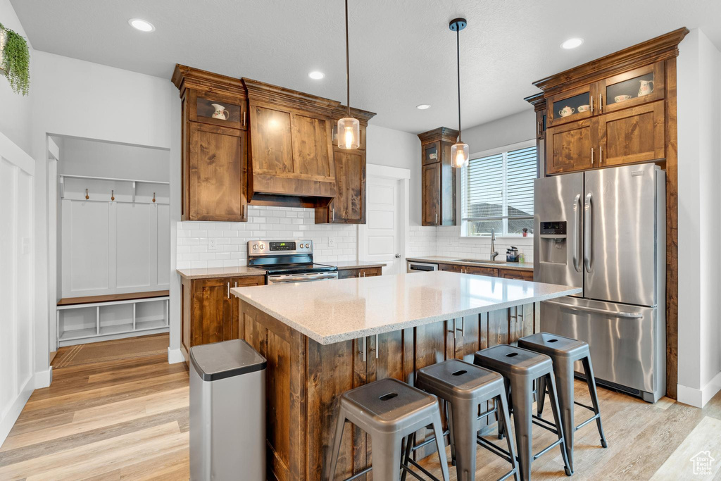 Kitchen featuring hanging light fixtures, a kitchen island, sink, light hardwood / wood-style floors, and stainless steel appliances