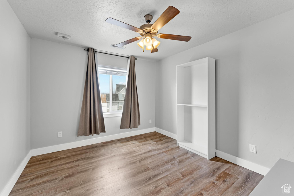 Empty room featuring ceiling fan, a textured ceiling, and light hardwood / wood-style flooring