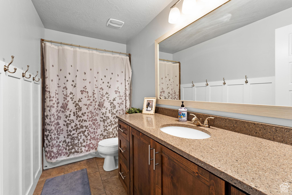 Bathroom featuring a textured ceiling, toilet, vanity, curtained shower, and tile patterned flooring