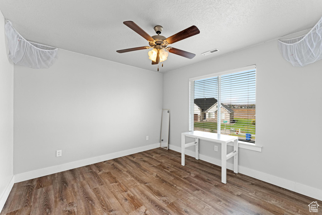 Empty room featuring a textured ceiling, wood-type flooring, and ceiling fan