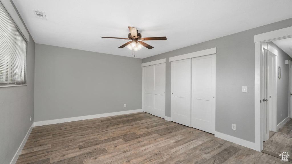 Unfurnished bedroom with hardwood / wood-style floors, multiple closets, and ceiling fan