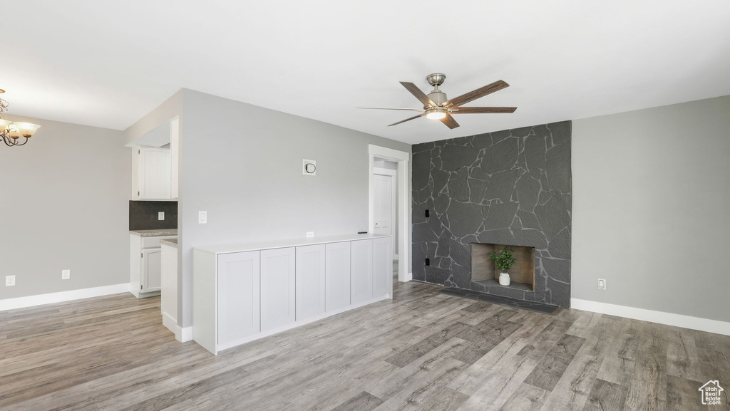 Unfurnished living room featuring a fireplace, ceiling fan with notable chandelier, and light wood-type flooring