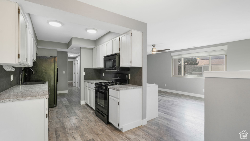 Kitchen with light hardwood / wood-style flooring, white cabinets, black appliances, and backsplash