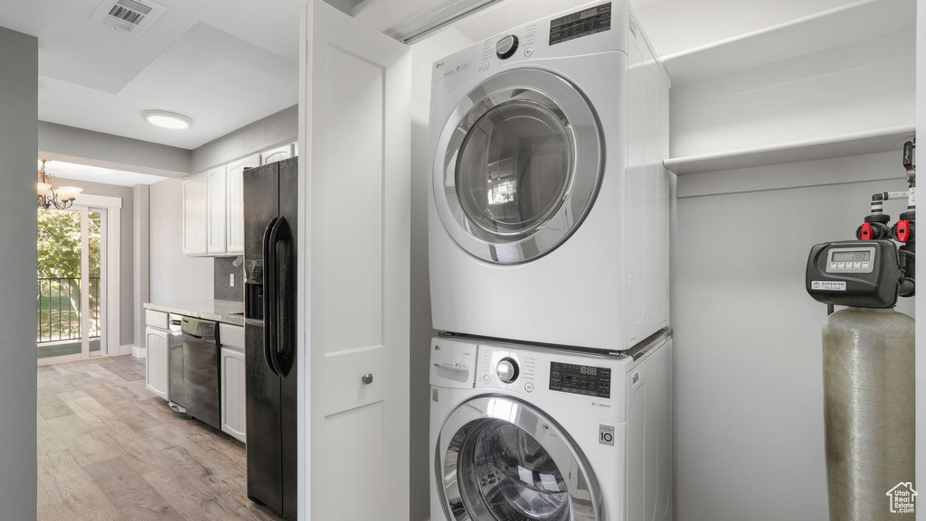 Laundry area featuring a notable chandelier, stacked washer and dryer, and light wood-type flooring