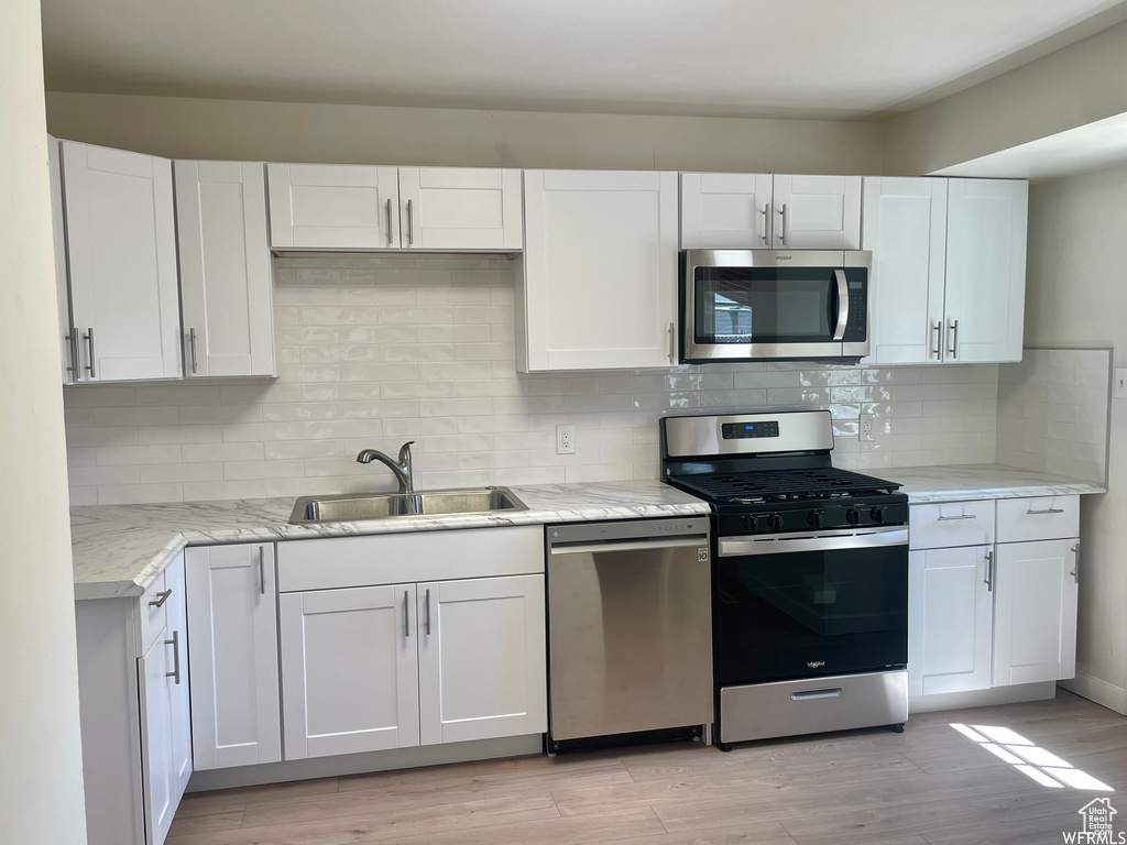 Kitchen with sink, white cabinetry, light hardwood / wood-style flooring, and stainless steel appliances