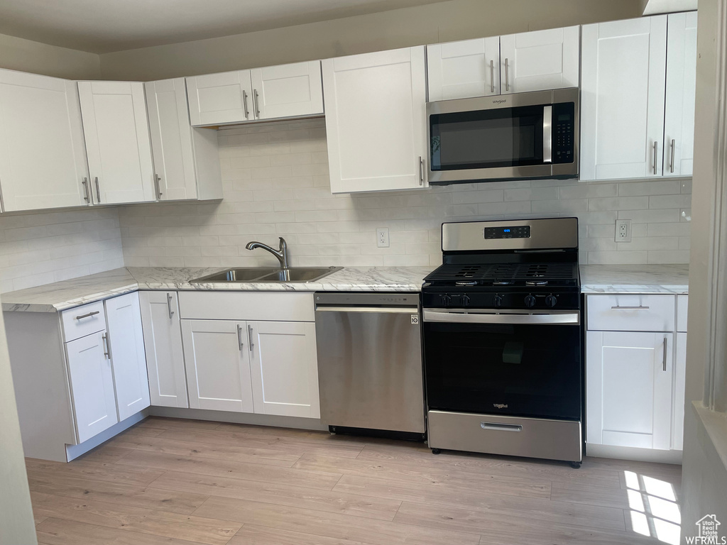 Kitchen with light stone counters, appliances with stainless steel finishes, white cabinetry, light hardwood / wood-style flooring, and sink