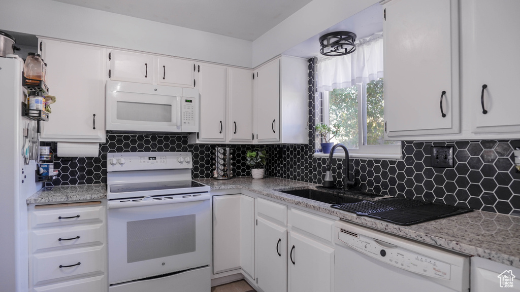 Kitchen with backsplash, white cabinets, light stone counters, and white appliances