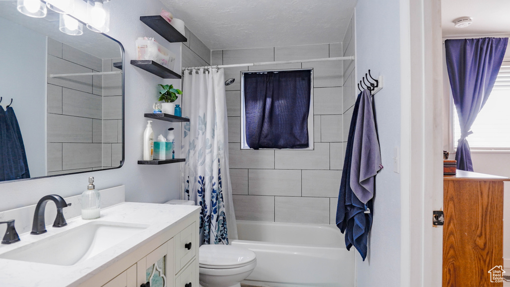 Full bathroom featuring toilet, shower / bath combo, vanity, and a textured ceiling