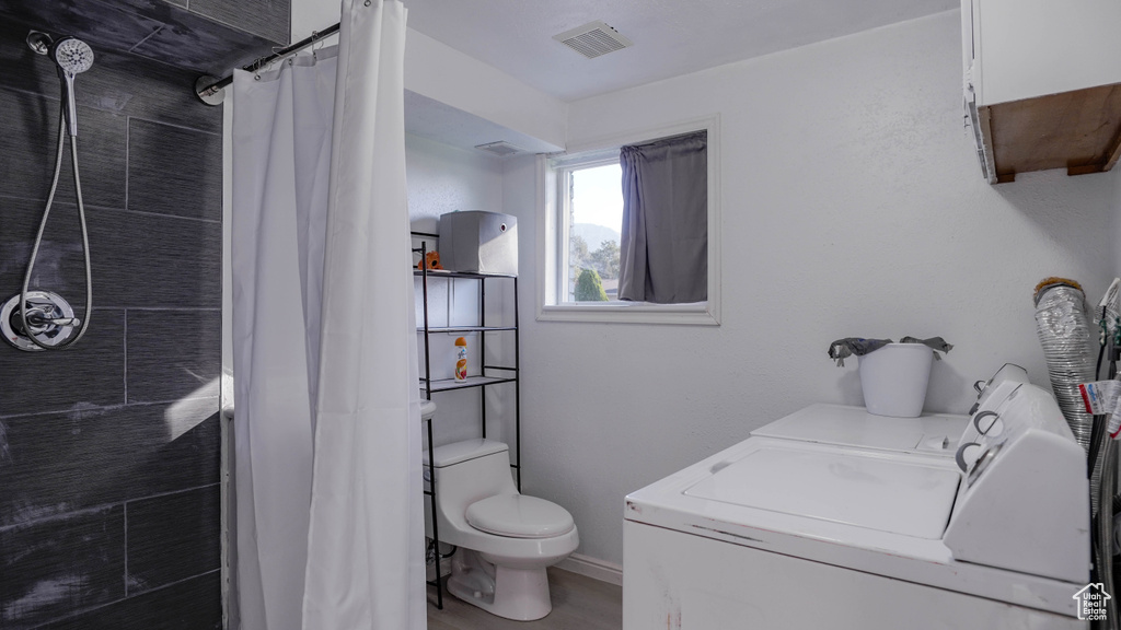 Bathroom featuring washing machine and clothes dryer, toilet, walk in shower, vanity, and hardwood / wood-style flooring