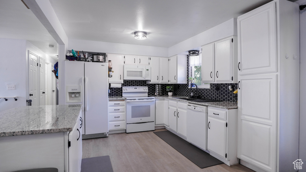 Kitchen featuring decorative backsplash, light hardwood / wood-style flooring, white cabinetry, light stone counters, and white appliances