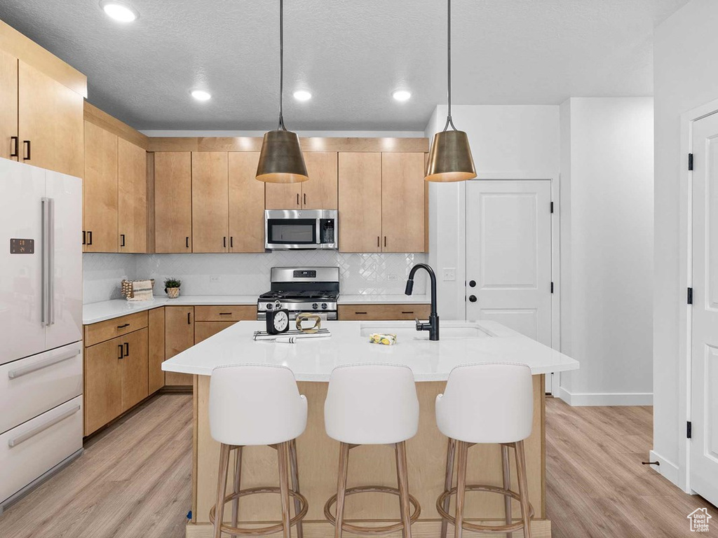 Kitchen with a center island with sink, hanging light fixtures, appliances with stainless steel finishes, and light hardwood / wood-style flooring