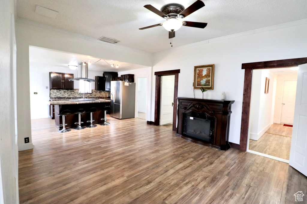 Living room with ceiling fan, a textured ceiling, light wood-type flooring, ornamental molding, and sink