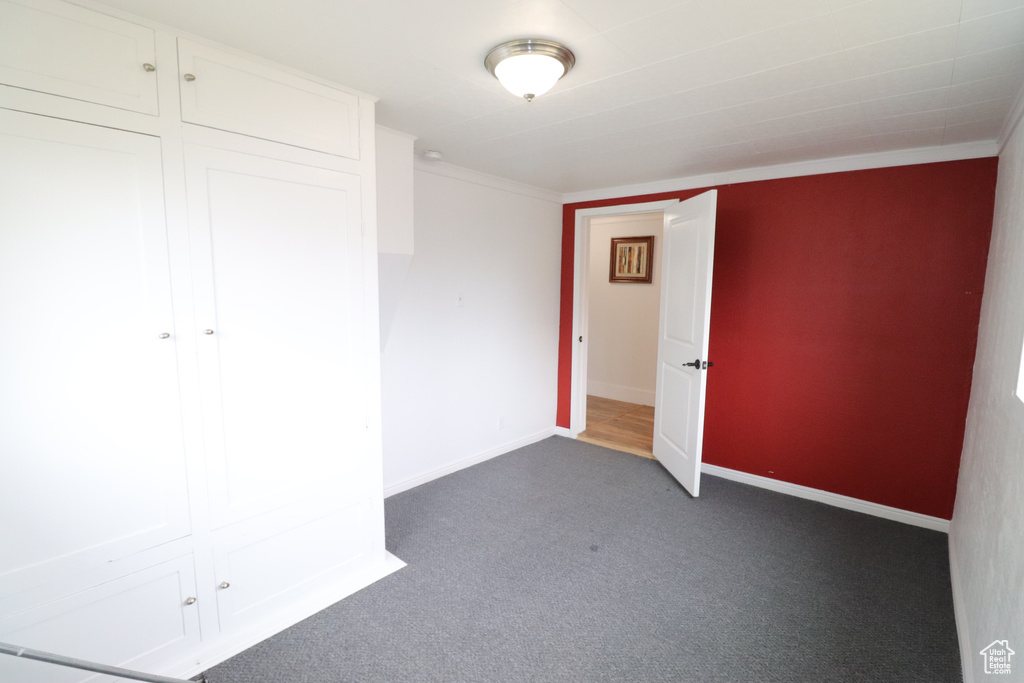 Unfurnished bedroom with a closet, ornamental molding, and dark carpet