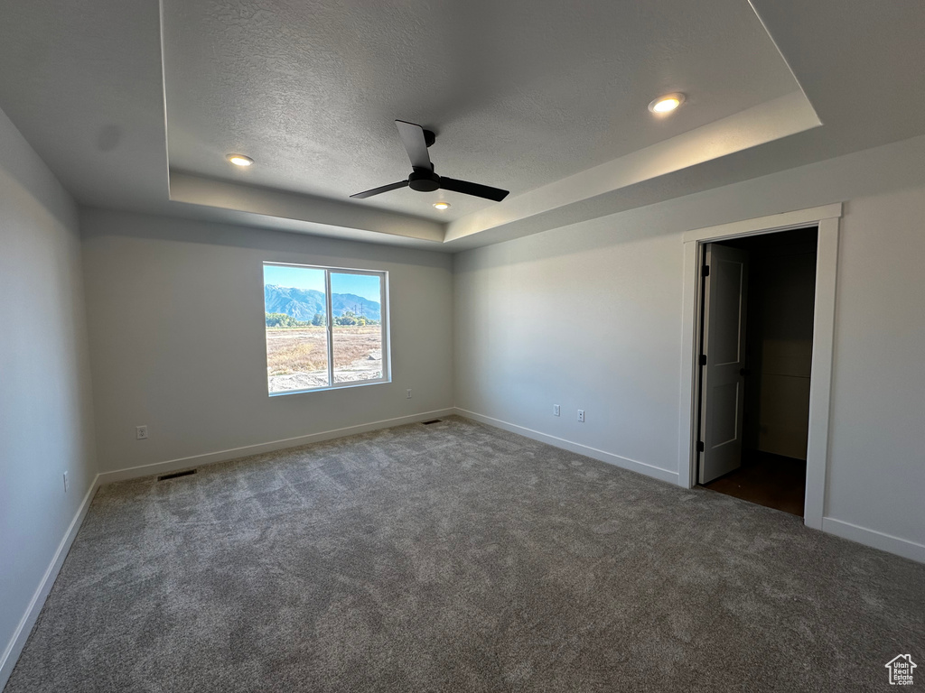 Carpeted empty room with ceiling fan, a textured ceiling, and a tray ceiling