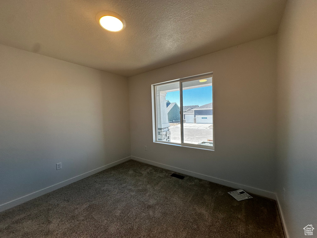 Empty room featuring dark colored carpet and a textured ceiling