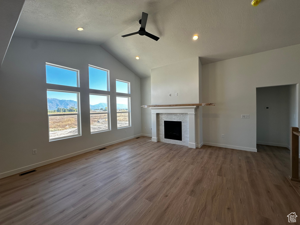 Unfurnished living room with a mountain view, wood-type flooring, vaulted ceiling, a textured ceiling, and ceiling fan