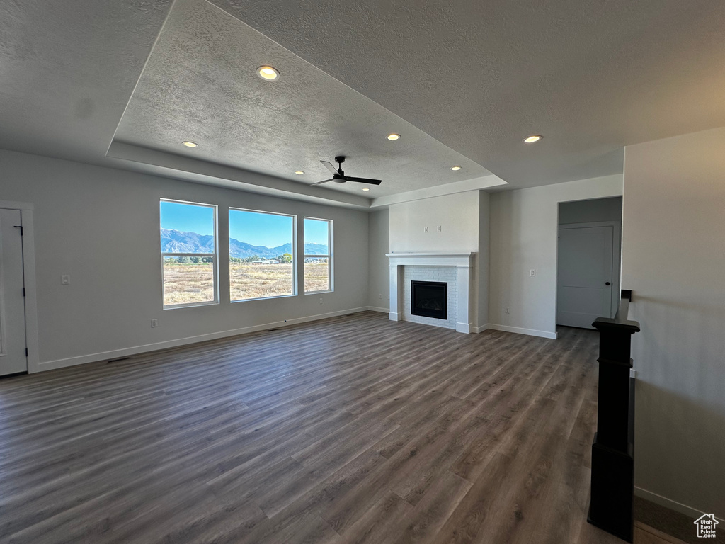 Unfurnished living room with dark hardwood / wood-style floors, a mountain view, a raised ceiling, a textured ceiling, and ceiling fan