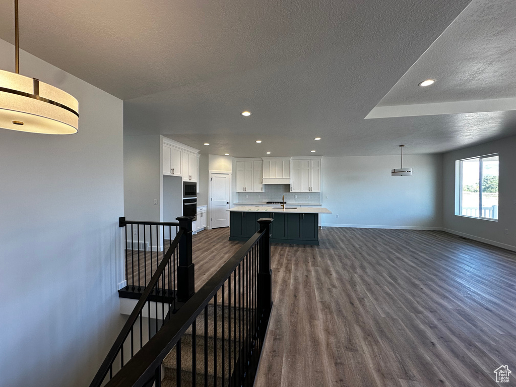 Kitchen featuring a textured ceiling, white cabinetry, a kitchen island with sink, dark hardwood / wood-style floors, and decorative light fixtures