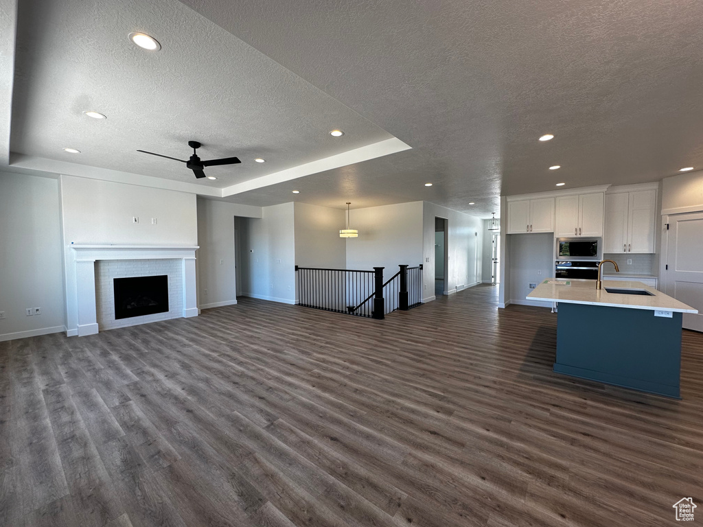 Unfurnished living room with sink, a textured ceiling, a tray ceiling, and dark hardwood / wood-style floors