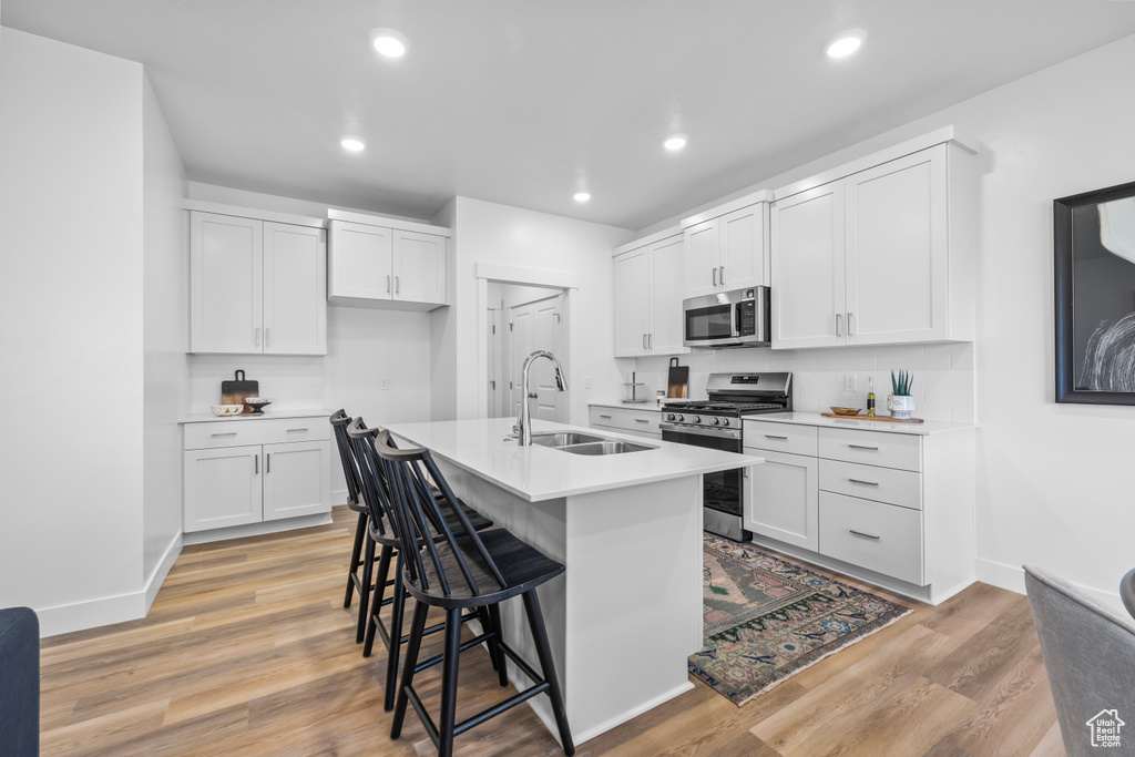 Kitchen featuring appliances with stainless steel finishes, sink, an island with sink, white cabinetry, and a breakfast bar area